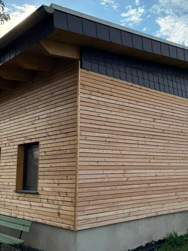 Hinterlüftete Holzfassade aus Lärchenleisten mit Kunstschiefer-Traufband